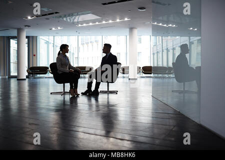 Certi giovani manager seduto di fronte a i suoi partner maschile mentre il brainstorming sul progetto comune, interni di dim spaziosa lobby di office su sfondo Foto Stock