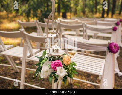 Floral elementi eleganti di decorazioni per matrimoni. Impostazioni per la romantica cerimonia di nozze al di fuori nella soleggiata foresta. Legno bianco sedie vuote decorate wi Foto Stock