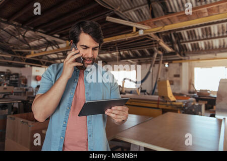 Falegname parlando sul suo cellulare e utilizzando un tablet Foto Stock