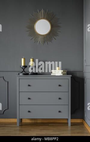 Armadietto grigio con oro candele e tre libri in piedi in dark room interno con uno specchio decorativo sulla parete con lo stampaggio Foto Stock