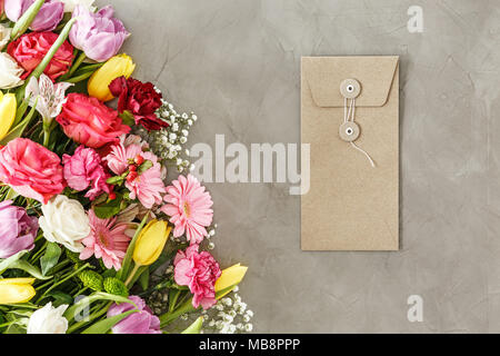 Busta marrone per un biglietto di auguri che giace su una tabella grigia accanto a un mazzo di fiori per la festa della mamma Foto Stock