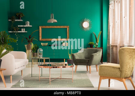 Tabella di rame sul tappeto e cornice dorata in living room interior verde con poltrona e divani beige Foto Stock