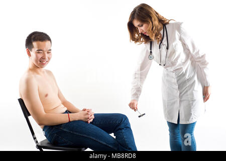 Ragazza medico controlla un nervoso riflesso in un paziente di East Asian aspetto (isolato su bianco) Foto Stock