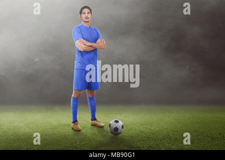 Bello asian giocatore di football con bracci incrociati sul campo in erba Foto Stock