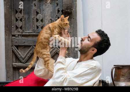 Giovani Musulmani uomo tenendo un gatto giallo di fronte ad una parete decorata Foto Stock