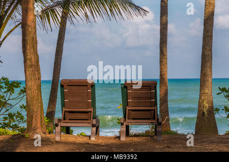 Una tipica vacanza bella scena con due sedie a sdraio, fiancheggiata da palme che offrono una fantastica vista sull'oceano della costa Est della Malaysia. Foto Stock