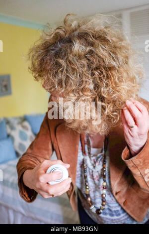 Persone di mezza età donna matura mediante spray per capelli sul biondo evidenziato i capelli ricci pronto per le ceneri serata fuori fotografia scattata da Simon Dack Foto Stock