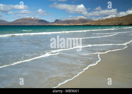 La laminazione delle onde sulla spiaggia deserta a Luskentire sull'Isle of Harris in primavera con la neve sulle colline in background. Foto Stock