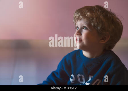 Splendida baby boy, capelli biondi e occhi blu, seduto a guardare in alto,copia di spazio. Foto Stock