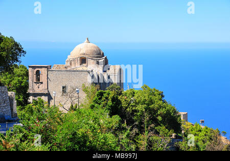 La Chiesa di San Giovanni Battista di posatoi sul versante di una montagna, nella cittadina medievale di Erice, in Sicilia. Tranquillo paesaggio verde, azzurro mare e cielo blu Foto Stock