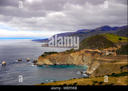 Vista aerea di Bixby Creek Bridge, Cabrillo Highway 1, California, Stati Uniti d'America. Il paesaggio costiero, Oceano Pacifico, il verde delle colline e grigio cielo cloud Foto Stock