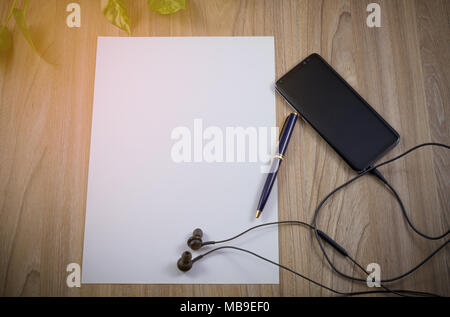 Smartphone, telefono cellulare, auricolare, bianco carta e penna sul tavolo di legno vista superiore con copia spazio, piatto sullo sfondo dei laici Foto Stock