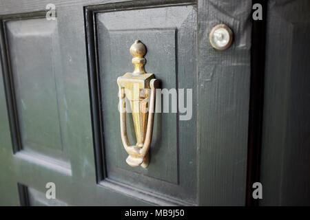 Porta in ottone respingente su un vecchio legno scuro della porta dipinta con pannelli in rilievo in una stretta fino angolo obliquo view Foto Stock