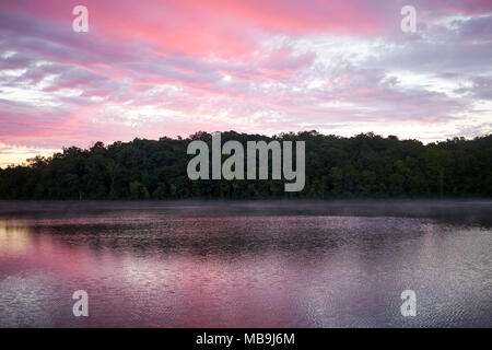 Rosa spettacolare tramonto riflesso in un tranquillo lago con vegetazione circostante e sulle basse colline in un paesaggio panoramico Foto Stock