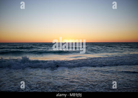 Vivido arancione tramonto tropicale al di sopra di un oceano calmo con piccole onde a Anna Maria Island, Florida come il sole affonda sotto l'orizzonte Foto Stock