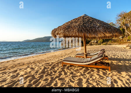 Lettini sotto ombrellone in spiaggia tropicale Foto Stock