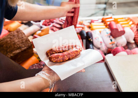 Donna di vendita in macelleria salsiccia tenuta avvolto nella carta Foto Stock