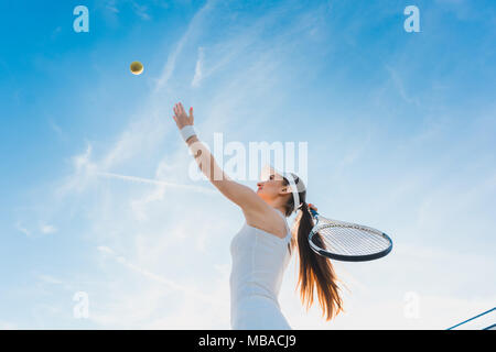 Donna giocando a tennis dando servizio Foto Stock