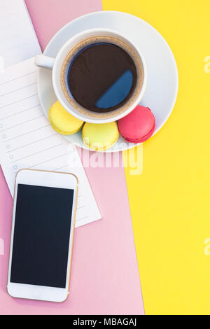 Piatti creativi foto laici della tazza di caffè con amaretti e un blocco note con copia spazio sul rosa e sfondo giallo stile minimal Foto Stock