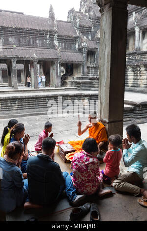 Un monaco buddista dando una benedizione a un cambogiano famiglia locale, Angkor Wat, Angkor Sito, Siem Reap, sito Patrimonio Mondiale dell'UNESCO, Cambogia, Asia Foto Stock