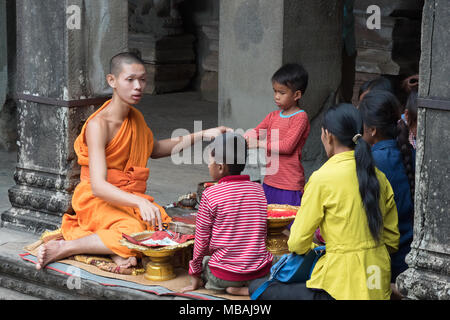 Un monaco buddista dando una benedizione a un cambogiano famiglia locale, Angkor Wat, Angkor Sito, Siem Reap, sito Patrimonio Mondiale dell'UNESCO, Cambogia, Asia Foto Stock