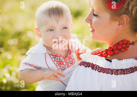 Ritratto di etnia famiglia ucraina indossando tradizionali vestiti di bianco. Giovane madre e bambino divertirsi al di fuori al sole estivo Campo di grano. Ve Foto Stock