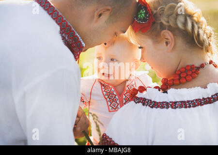 Ritratto di etnia famiglia ucraina indossando tradizionali vestiti di bianco. Il padre, la madre e il bambino più piccolo avendo divertimento fuori al sole estivo campo. Horizo Foto Stock