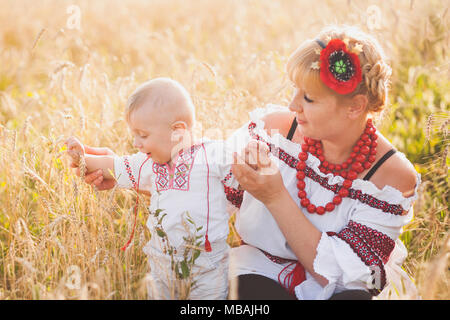 Ritratto di etnia famiglia ucraina indossando tradizionali vestiti di bianco. Giovane madre e bambino divertirsi al di fuori al sole estivo Campo di grano. Ve Foto Stock