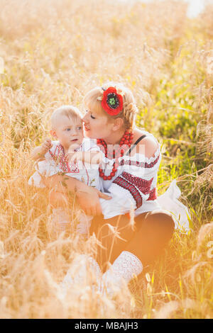 Ritratto di etnia famiglia ucraina indossando tradizionali vestiti di bianco. Giovane madre e bambino divertirsi al di fuori al sole estivo Campo di grano. Ve Foto Stock