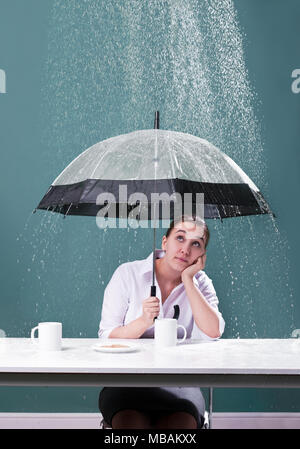 Donna seduta a un tavolo con ombrellone sotto la pioggia Foto Stock