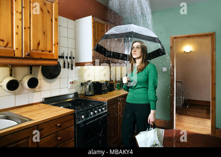 Donna in piedi in cucina con ombrello sotto la doccia di pioggia, in interni Foto Stock