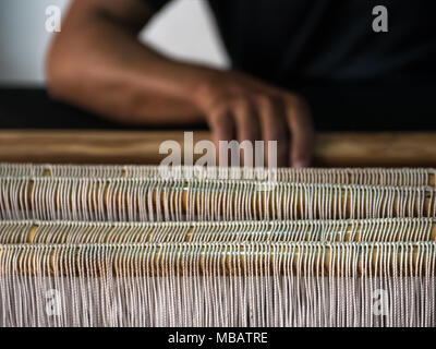 Un tessitore dimostra la tessitura sul suo telaio in un souk di Marrakech, Marocco. Il focus è sul thread in tessuto con la sua mano in background. Foto Stock
