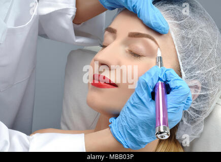 Microblading sopracciglia. Cosmetologo rendendo trucco permanente. Donna attraente getting cura facciale e tatuaggio al salone di bellezza Foto Stock