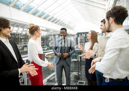 Due uomini di affari si stringono la mano mentre i loro colleghi applaudendo e sorridente Foto Stock