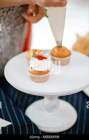 Processo di topping tortine con crema utilizzando una sacca di tela da pasticceria. Foto Stock