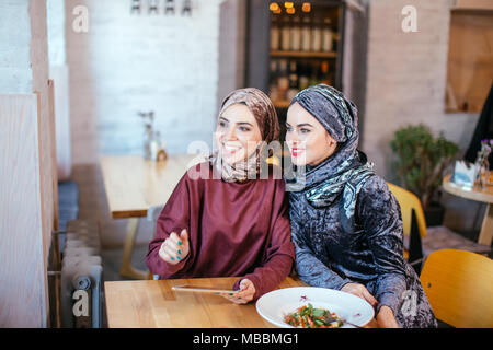 Due donne musulmane in cafe, shop online utilizzando la tavoletta elettronica Foto Stock