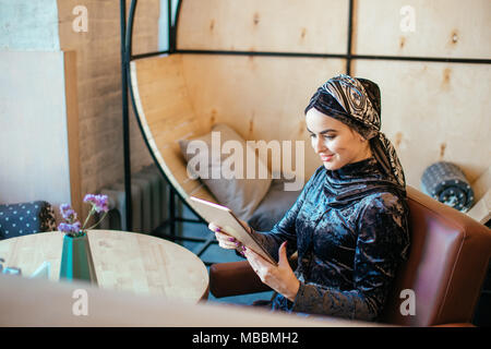 Bella arabo musulmano ragazza utilizzando tablet in cafe Foto Stock