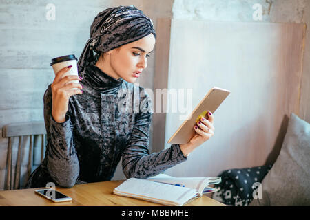 Le donne musulmane lavora con tablet e bere un caffè nella caffetteria Foto Stock