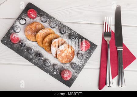 Mini pancake con frutta e miele su una piastra con tè e miele in background Foto Stock