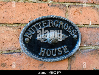 Smart ornato di forma ovale in metallo fuso segno casa per casa Buttercross montato sul vecchio rosso muro di mattoni, Oakham, Rutland, Leicestershire, England, Regno Unito Foto Stock