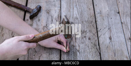 Le donne la mano è mantenere il martello e di guidare un chiodo è sdraiato su un tavoli in legno nero. Copia dello spazio. Foto Stock