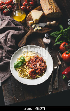 La pasta italiana con salsa di pomodoro, gamberi e parmigiano su tavola in legno rustico. Immagine dai toni, il fuoco selettivo, tabella vista superiore Foto Stock