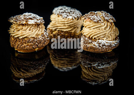 Tre francese dessert shoo con caramello ripieno di panna servita su specchio nero lo sfondo con la riflessione Foto Stock