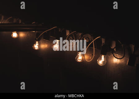 Il vecchio stile ghirlanda di vintage Tungsten bulb lampade pendenti sulla parete scura di notte. Close up foto con messa a fuoco selettiva Foto Stock