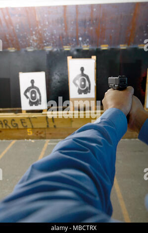 L'uomo, eventualmente un funzionario di polizia, facendo pratica di bersaglio in un poligono di tiro con una pistola visto da dietro lungo i suoi bracci estesi come egli prende la mira Foto Stock