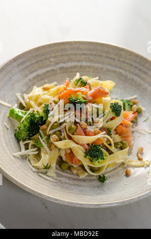 Italian tagliatelle con tagli fritto di filetti di salmone, broccoli, piselli e aneto in piastra ceramica Foto Stock