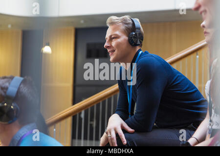 Sorridendo, uomo attento ascolto delle cuffie nel pubblico di conferenza Foto Stock