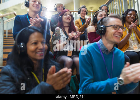 Udienza sorridente con cuffie battendo le mani a una conferenza Foto Stock