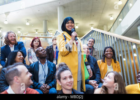 Donna sorridente in hijab parlando con microfono in udienza di conferenza Foto Stock