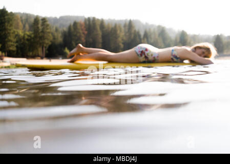 Serena donna recante sulla paletta board sul tranquillo lago Foto Stock